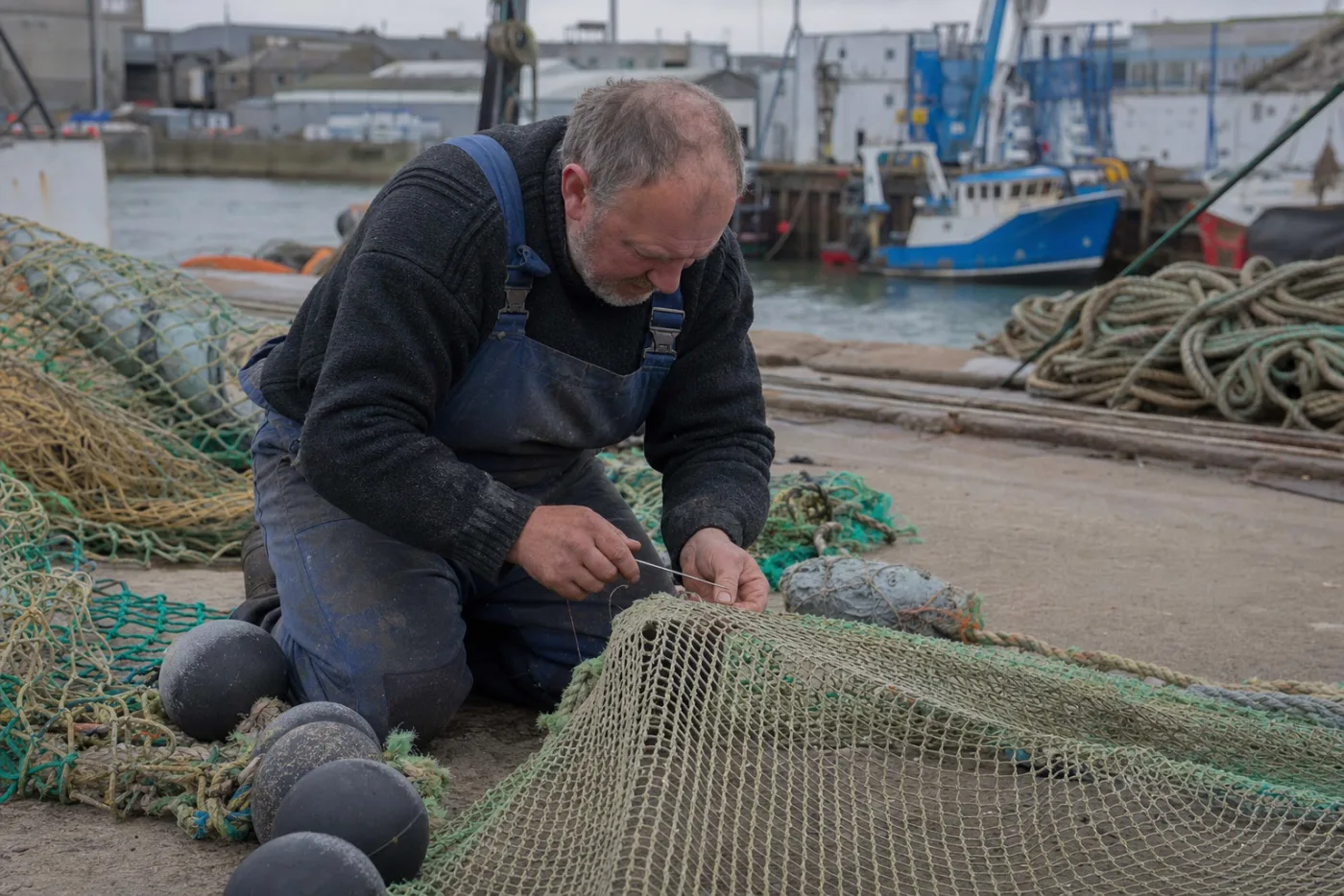 A netmaker mending a trawl net on a harbour quay